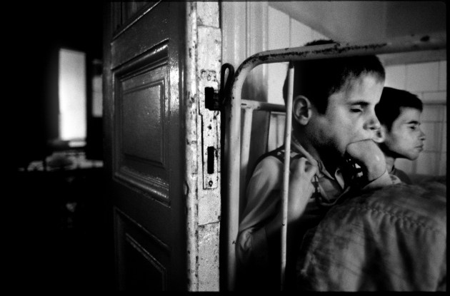 © William Snyder. A teenage girl suffering from some unknown set of physical and mental illnesses sits in her bed with her female teenage companion in the Home for Irrecoverables in Gradinari, Romania. May, 1990. This image is one of 12 images that won the 1991 Pulitzer Prize for Feature Photography.